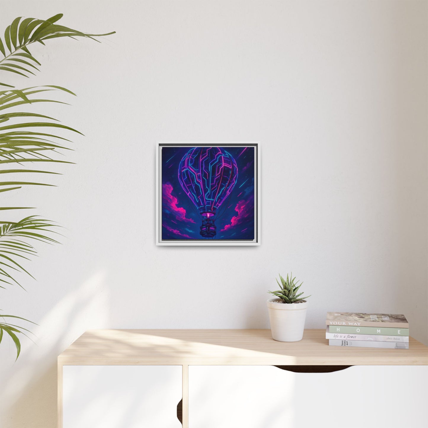 Framed abstract art piece on a wall above a desk with a plant and books.