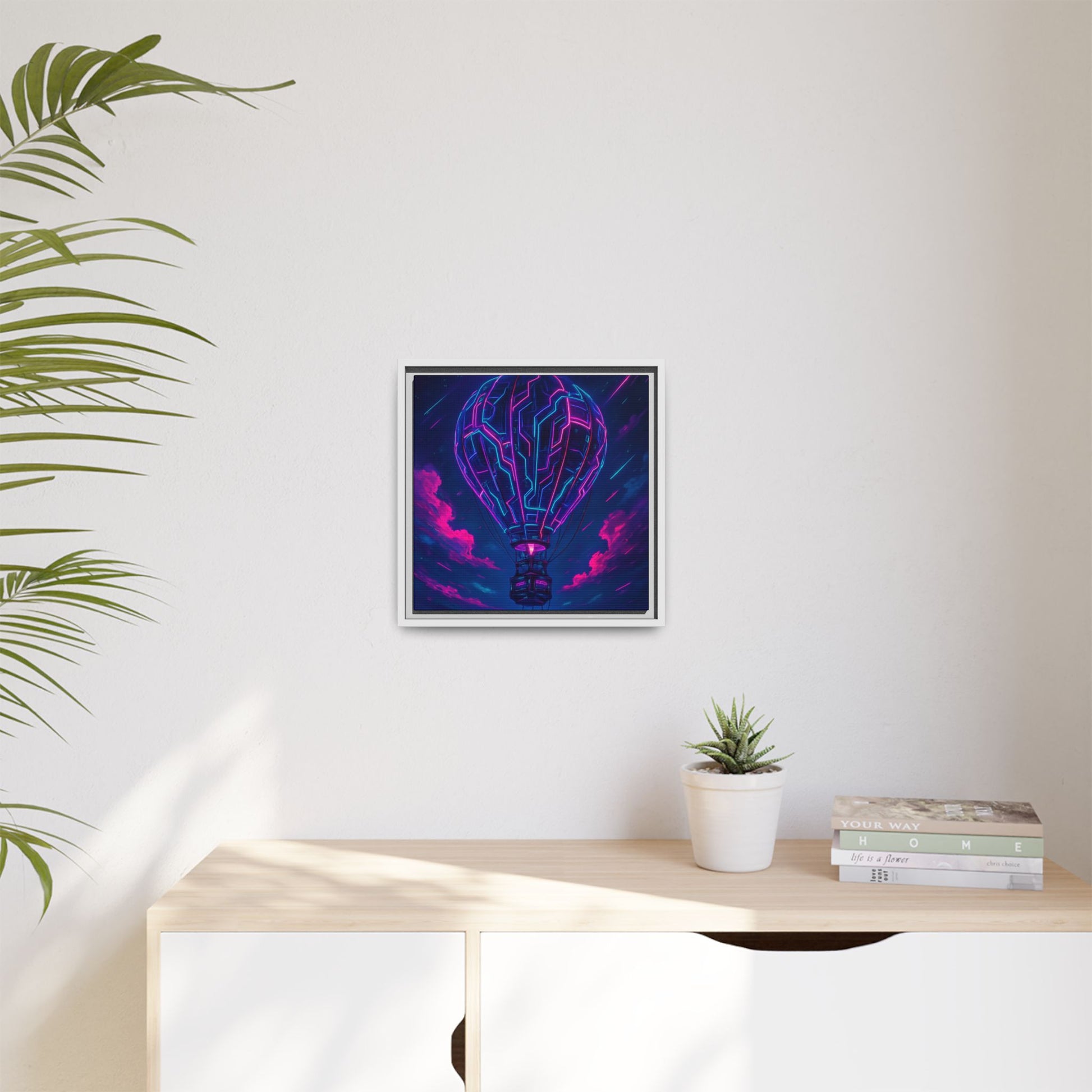 Framed abstract art piece on a wall above a desk with a plant and books.